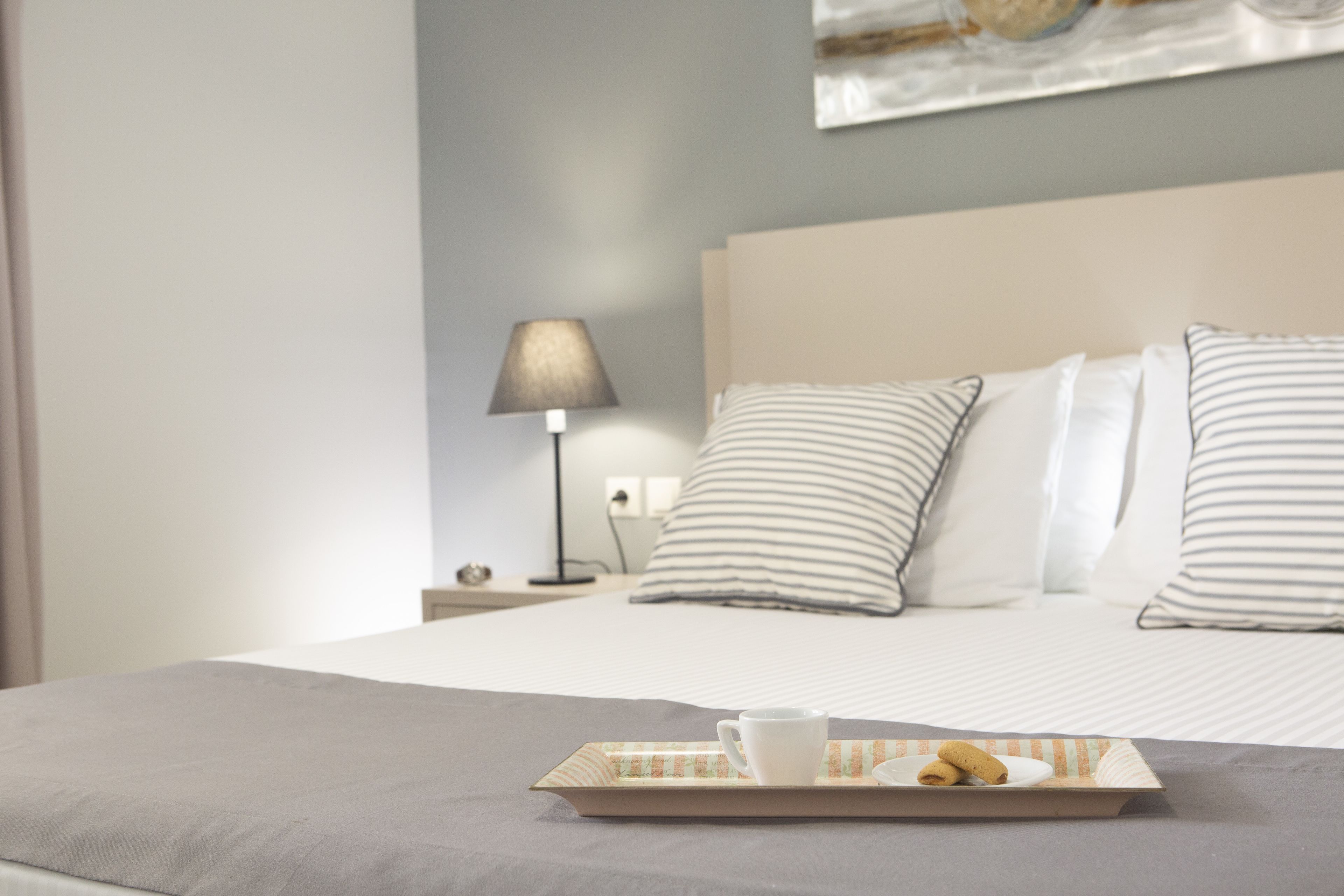 A neatly made bed with striped pillows, a bedside lamp, and a tray with a cup and pastries on the bed.