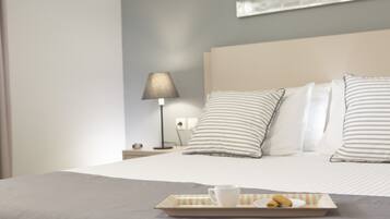 A neatly made bed with striped pillows, a bedside lamp, and a tray with a cup and pastries on the bed.
