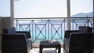 A balcony with wicker furniture and a table, overlooking a body of water and distant hills.