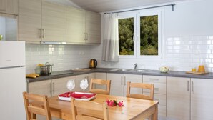 A modern kitchen with wooden cabinets, a dining table with chairs, and a window with a view of trees. - Captain Nick (Lefkada)
