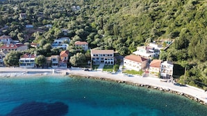 An aerial view of a coastal residential area with houses, a clear blue sea, and a rocky shoreline. - Captain Nick (Lefkada)