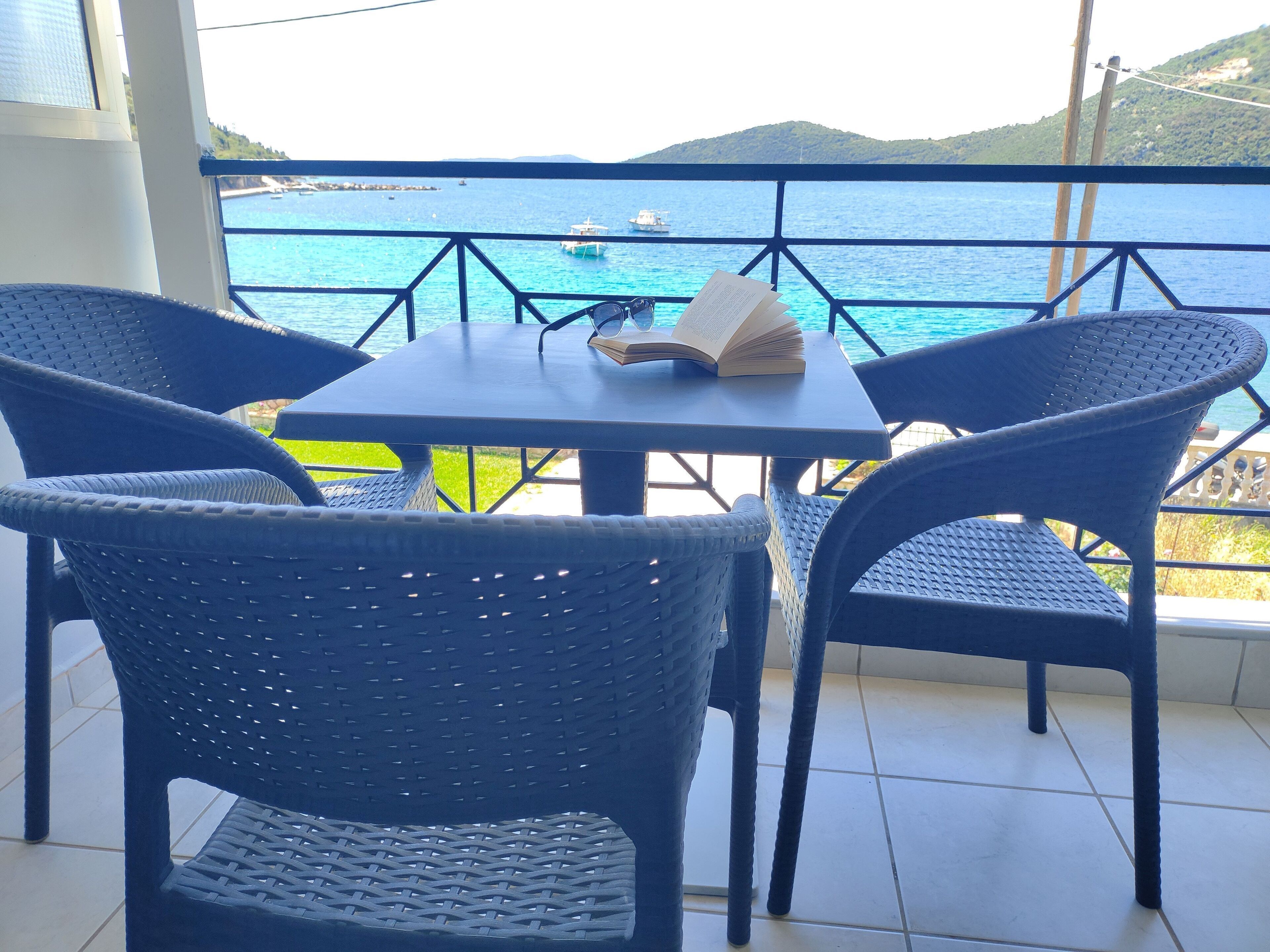 A balcony with a table and chairs, overlooking a body of water with boats.