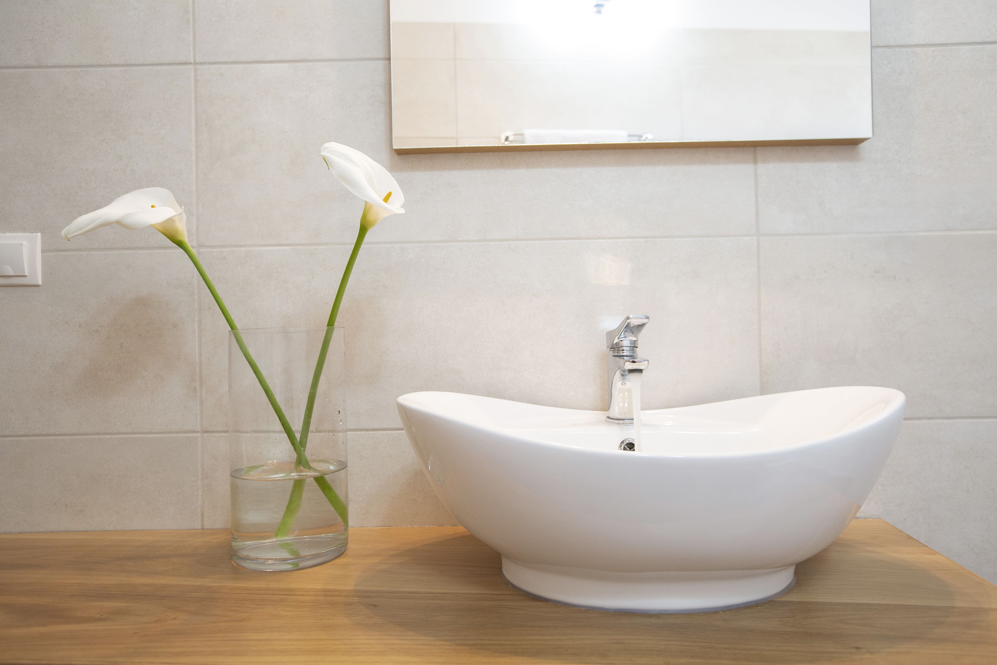 A bathroom with a white sink and a glass vase with two white flowers.