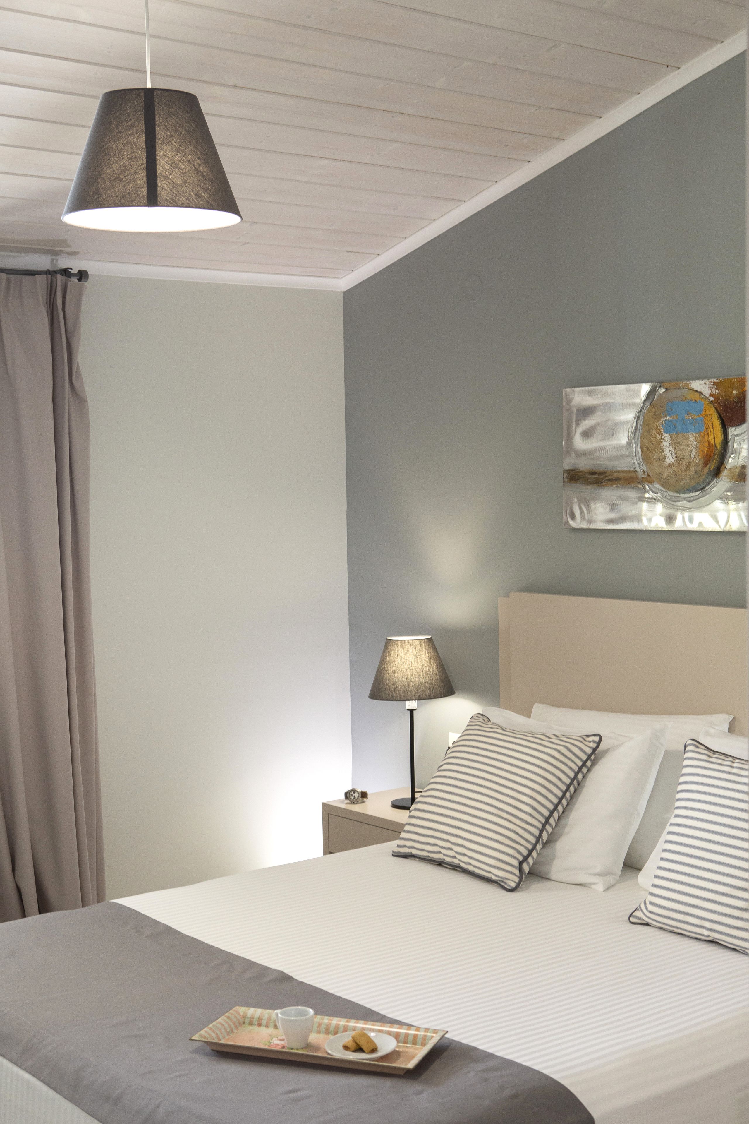 Un letto rifatto con cura, un vassoio con biscotti e una tazza, una lampada da comodino e un quadro appeso al muro.