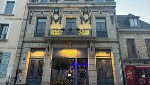 A historic building with ornate ironwork, a central entrance with a blue-lit glass door, and a sign indicating it is a hotel. - Hôtel Vintage (Quimperle)
