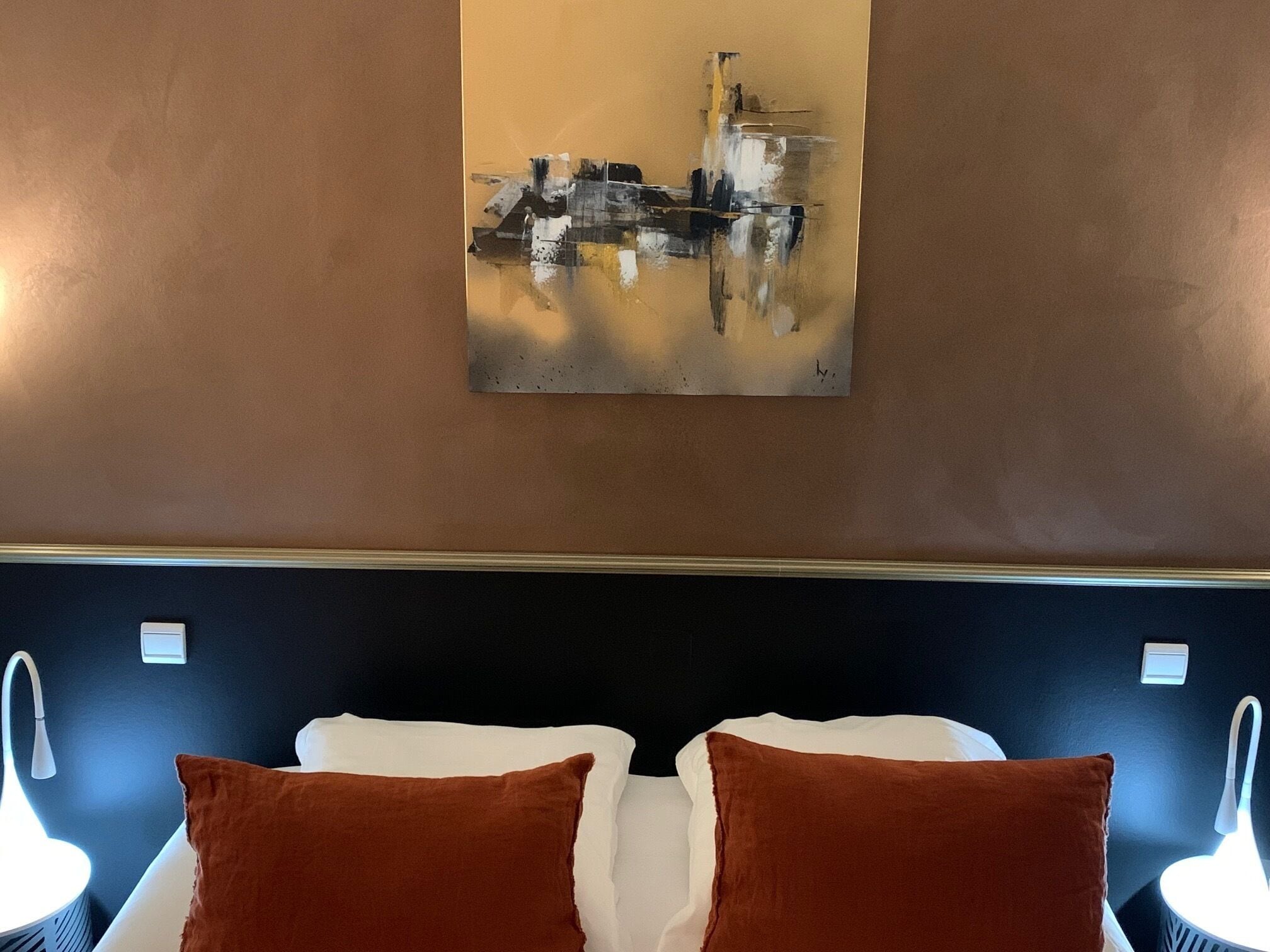 Ett hotellrum med en säng, två kuddar, en tavla som hänger på väggen och sänglampor.