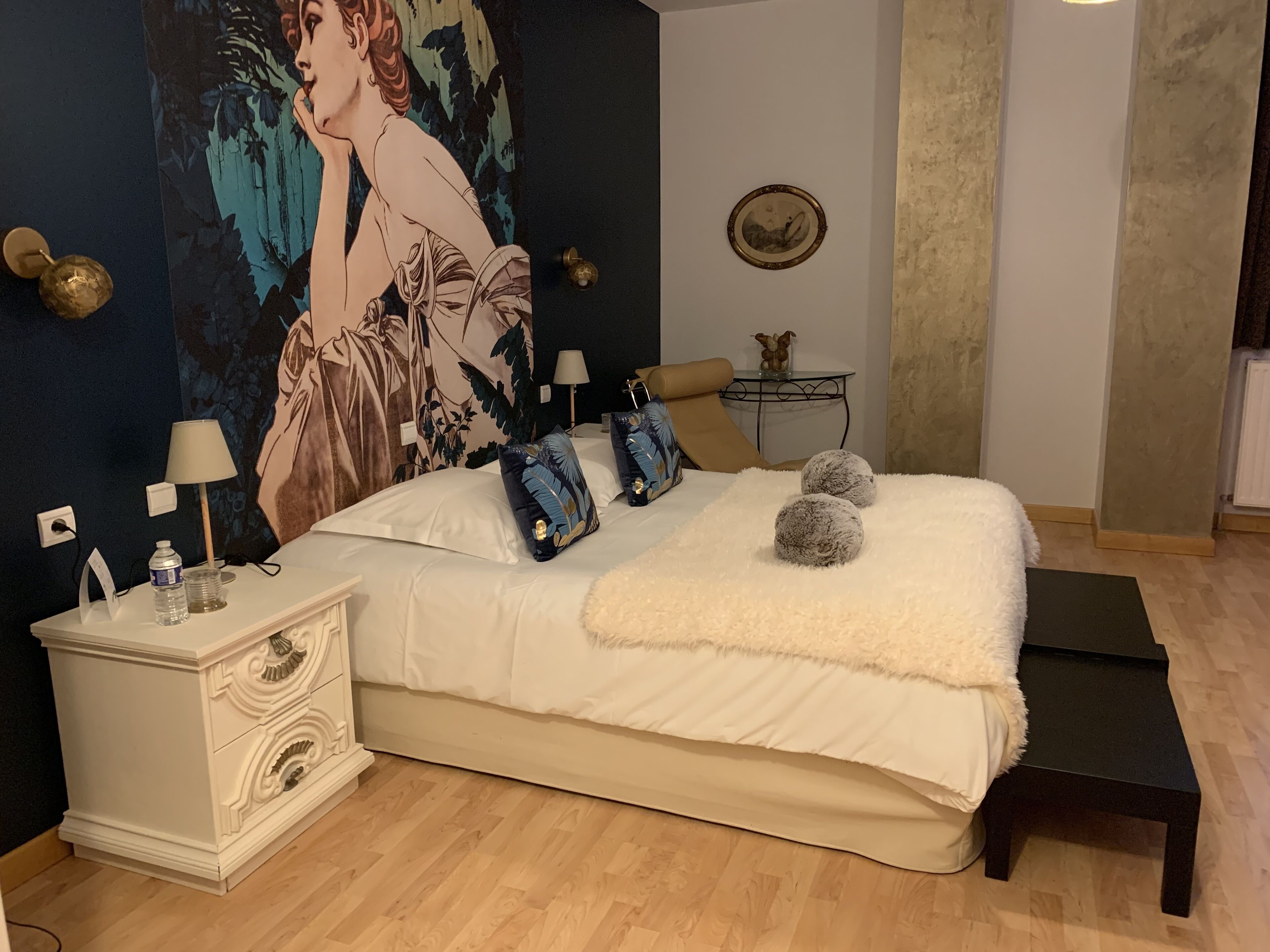 Un dormitorio con una cama grande, mesitas de noche, lámpara, cojín decorativo, manta suave y un cuadro en la pared.
