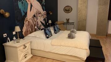 Un dormitorio con una cama grande, mesitas de noche, lámpara, cojín decorativo, manta suave y un cuadro en la pared.