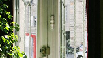 Una ventana con herrajes decorativos y vistas a una puerta roja y edificios al exterior.