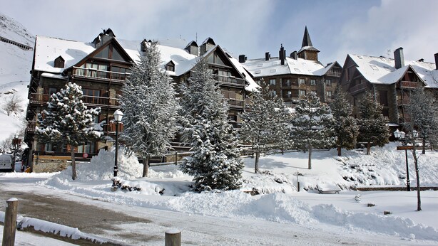 A snow-covered lodge with multiple balconies and a ski slope in the background.