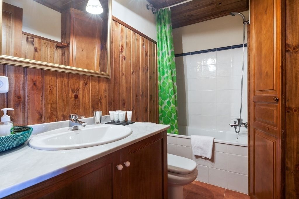 A bathroom with wooden paneling, a white sink, a toilet, and a shower with a green curtain.