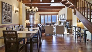 A spacious living area with a wooden ceiling, a dining table with chairs, a sofa, and a staircase.