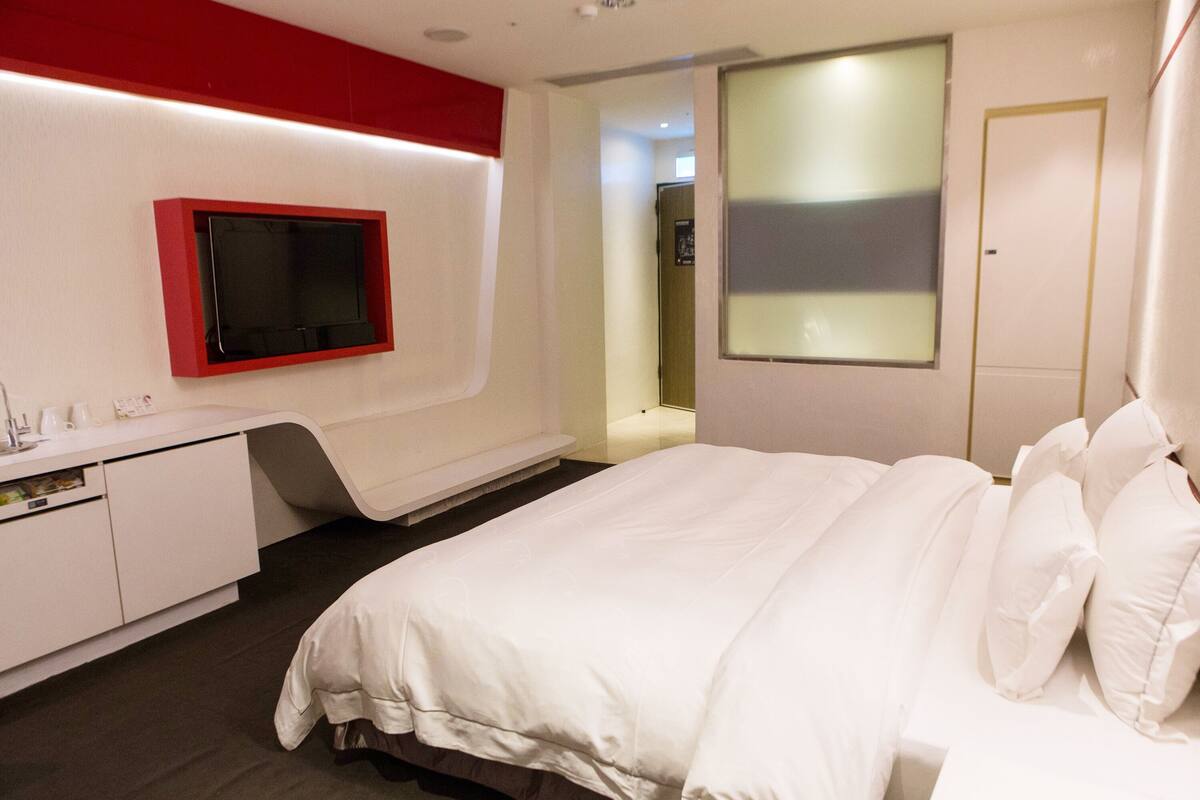Ein modernes Hotelzimmer mit einem Bett, einem Schminktisch mit Spiegel und einem an der Wand befestigten Fernseher.
