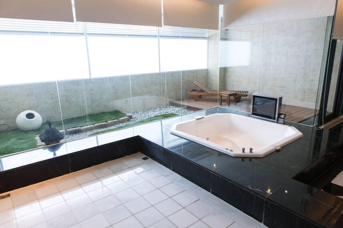 Ein modernes Badezimmer mit einer großzügigen Badewanne, einer kleinen Sitzecke und Gartenblick durch große Fenster.