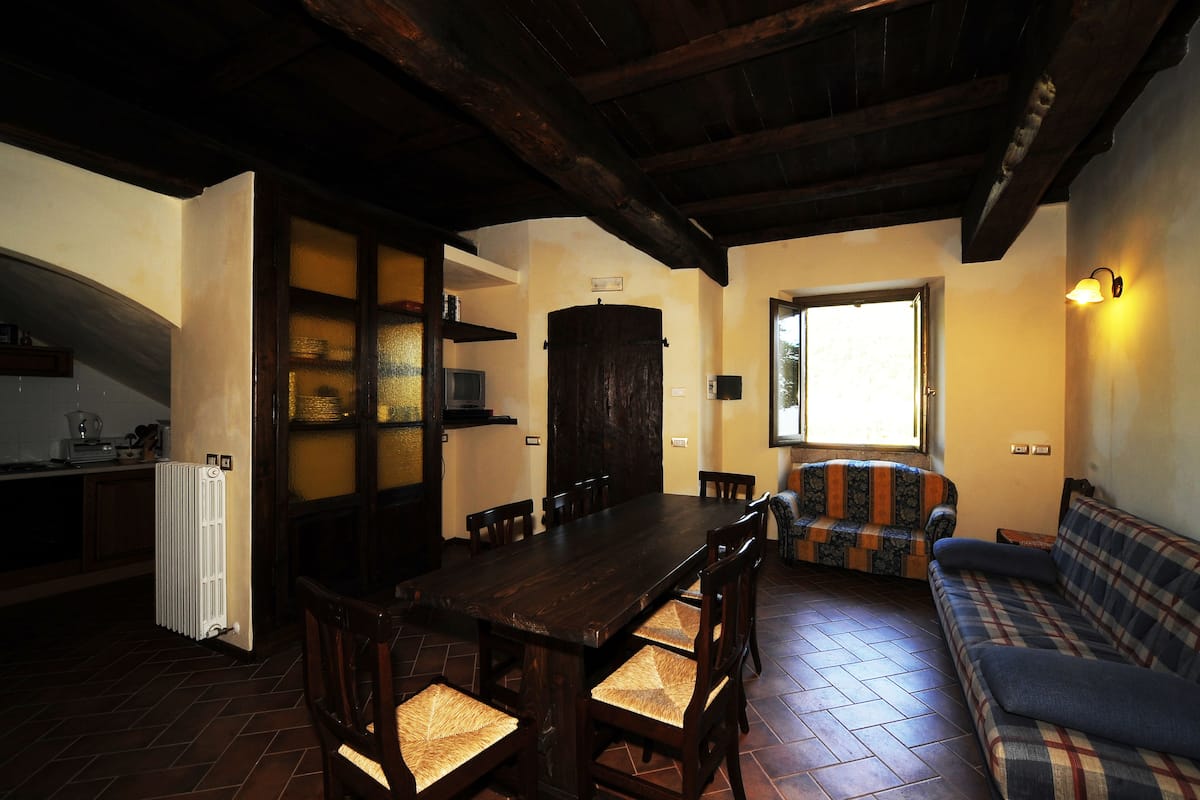 Uma sala de estar acolhedora com uma mesa de jantar de madeira escura, um sofá e uma televisão.