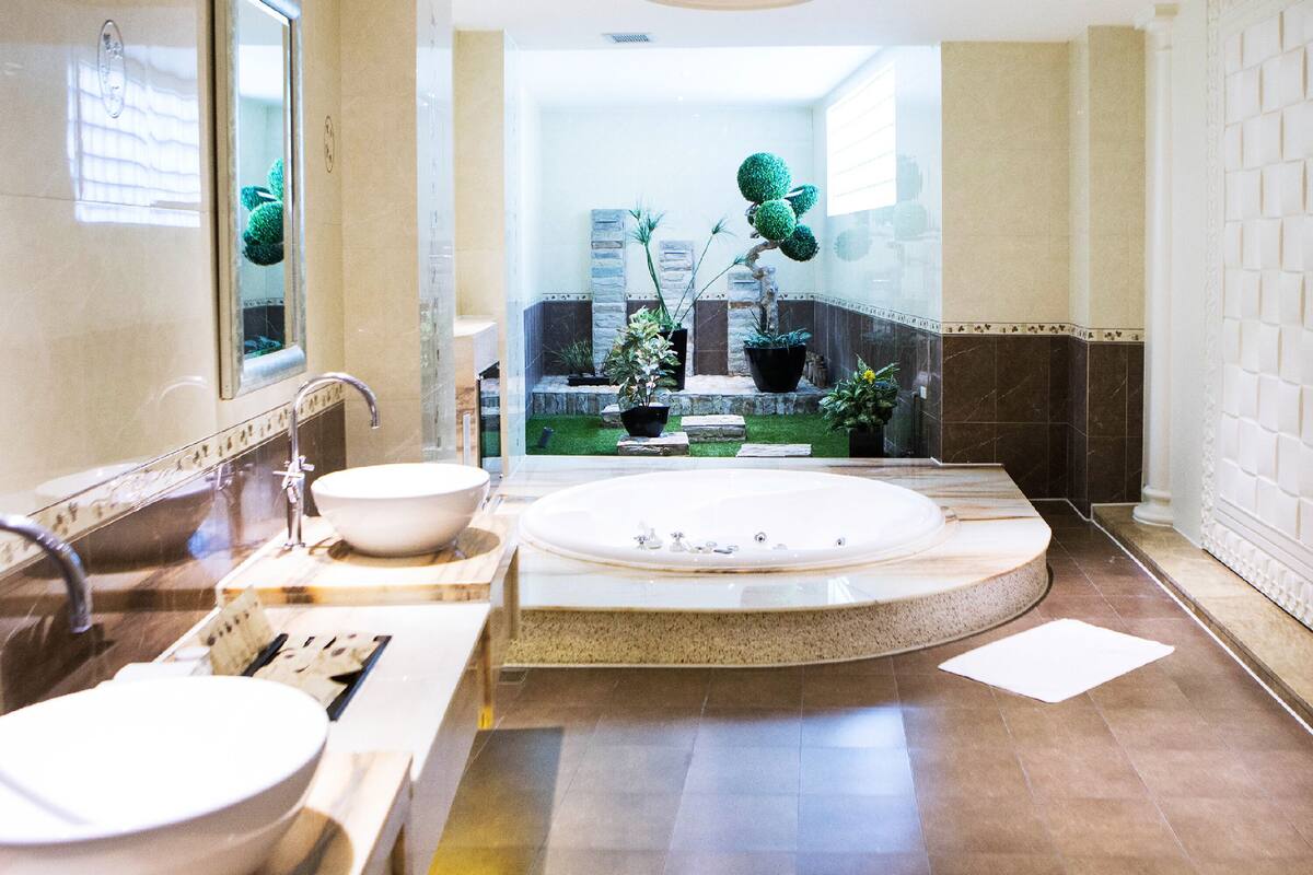A modern bathroom with a large bathtub, two sinks, and a small garden area visible through a glass door.