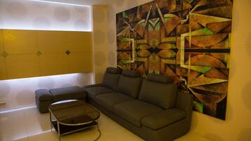 A modern living room with a sectional sofa, a glass coffee table, and a large abstract painting on the wall.
