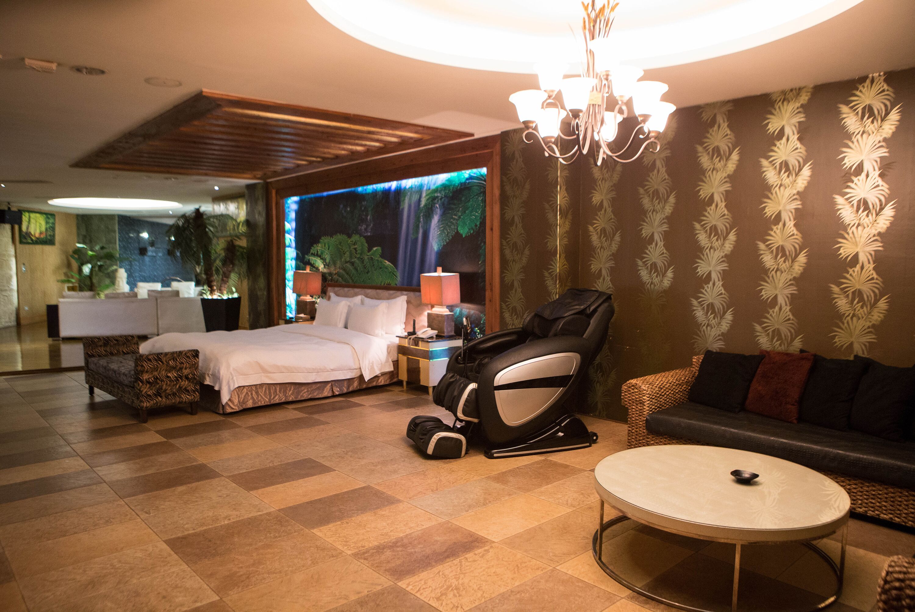 Una habitación de hotel con cama, sillón de masaje, sofá y una mesa redonda.