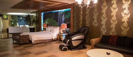Una habitación de hotel con cama, sillón de masaje, sofá y una mesa redonda.