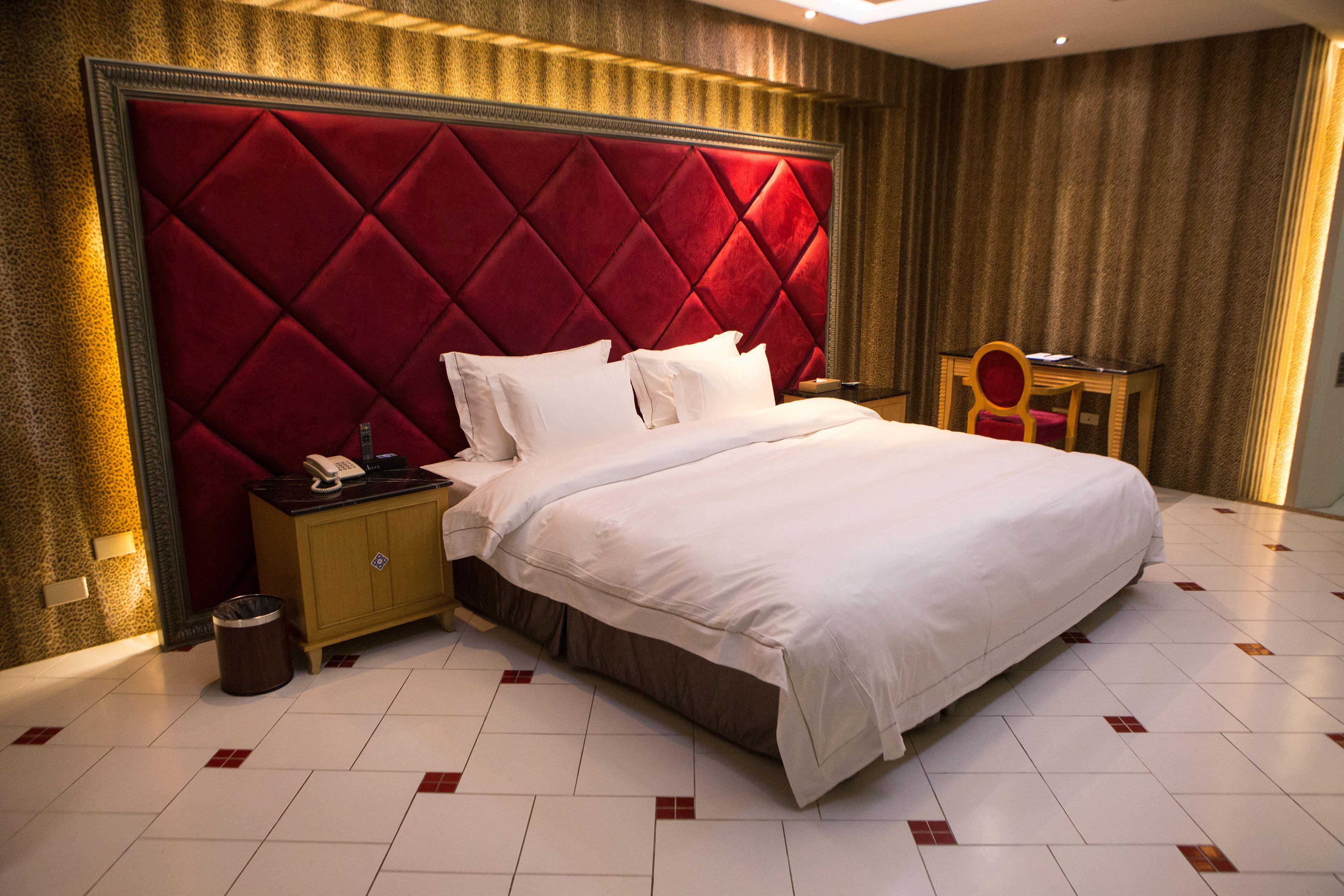 A hotel room with a large bed, a nightstand, a telephone, and a small table with a chair.