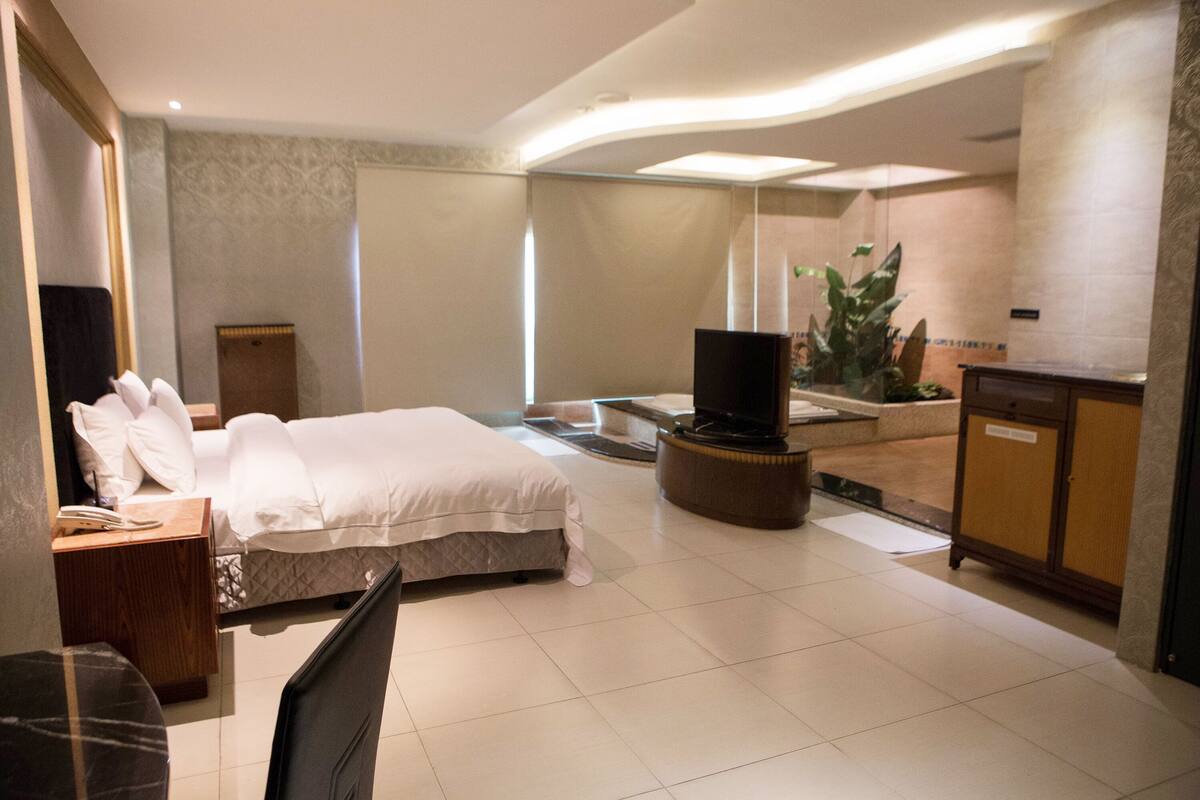 A modern hotel room with a large bed, a TV, a desk, and a cabinet.
