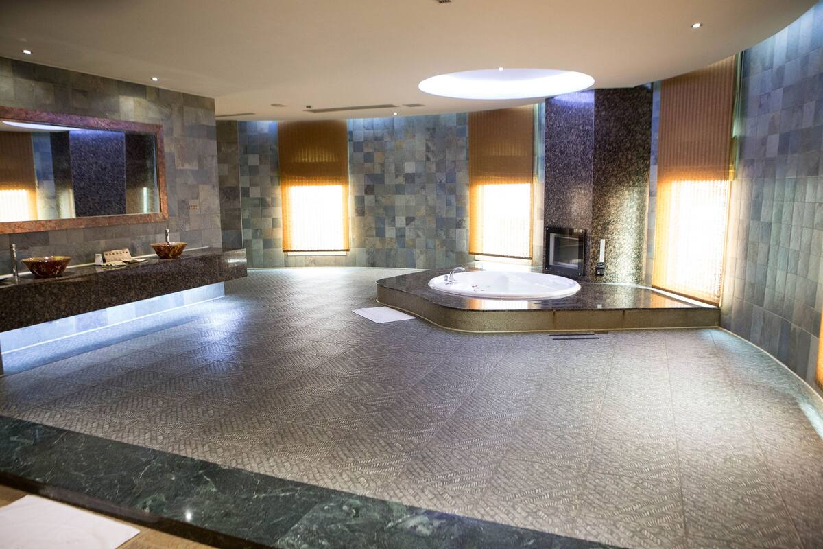 A spacious bathroom with a large bathtub, a vanity with a mirror, and a tiled floor.
