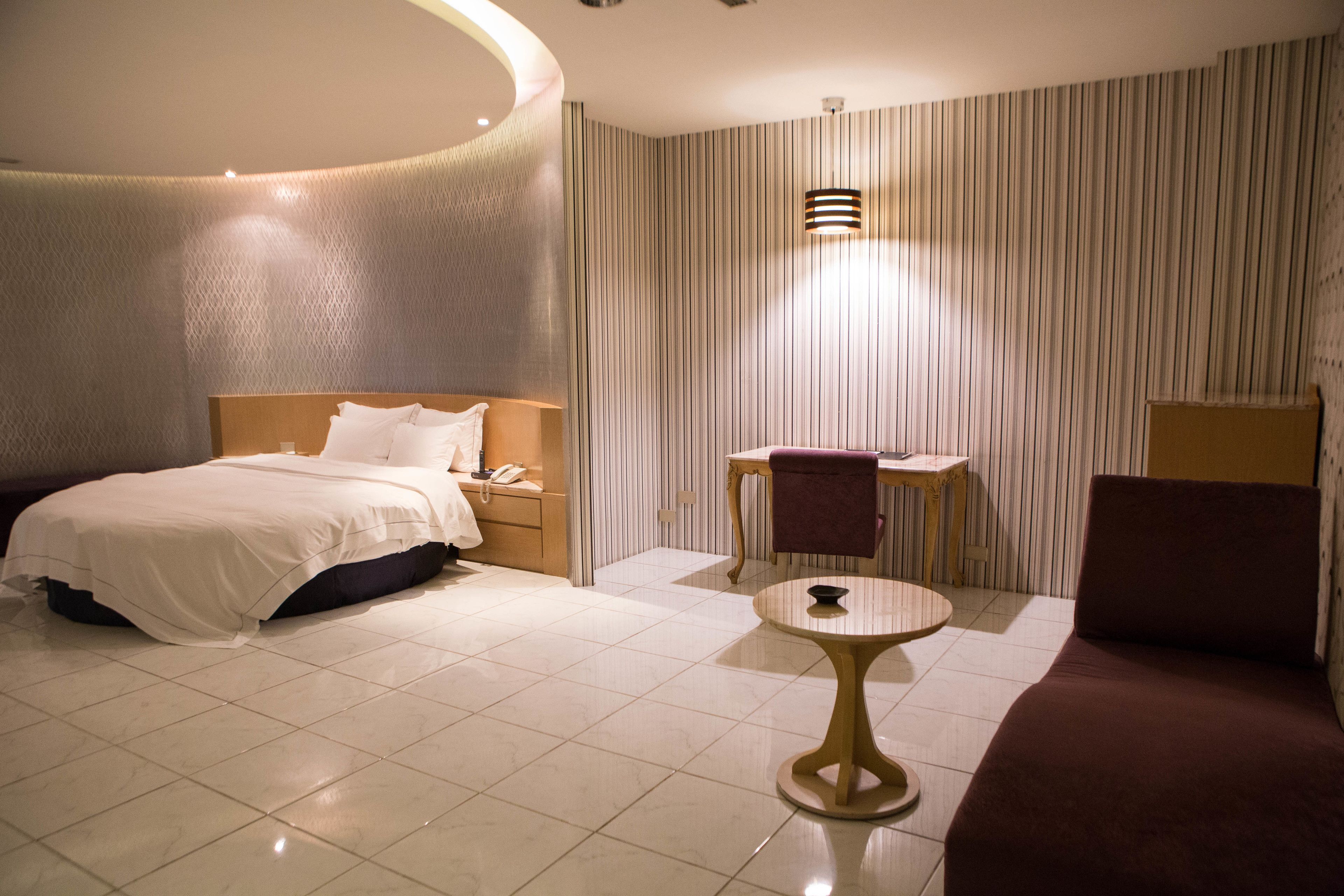 A hotel room with a bed, a small round table, a chair, and a desk with a chair.
