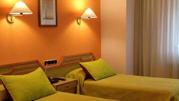 Habitación de hotel con dos camas, cada una con un almohadón verde, una mesita de noche y dos lámparas fijadas a la pared.