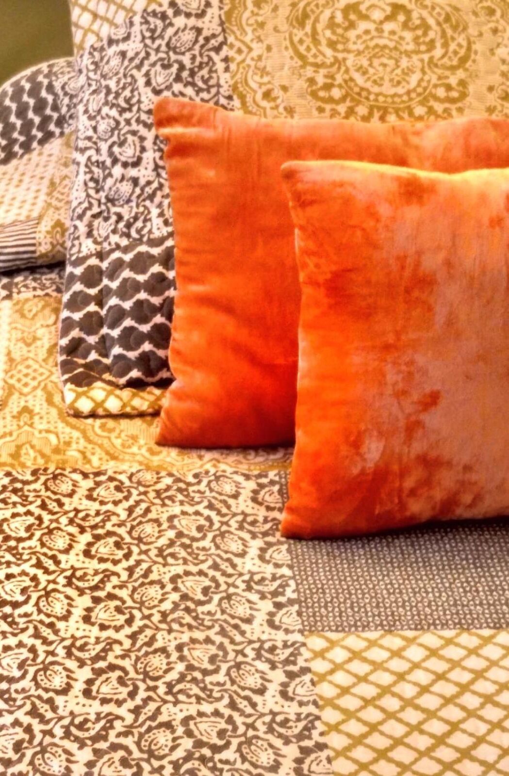 A bed with a patterned bedspread and two orange pillows.