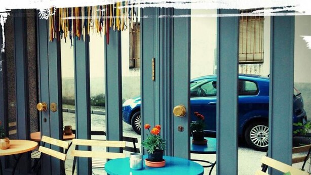 An outdoor seating area with tables and chairs, a blue car parked in the background, and a building with vertical columns. - Hotel Torres (Guijuelo)