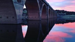 A bridge with multiple arches over a calm body of water, reflecting the structure and the sky. - Hotel Torres (Guijuelo)