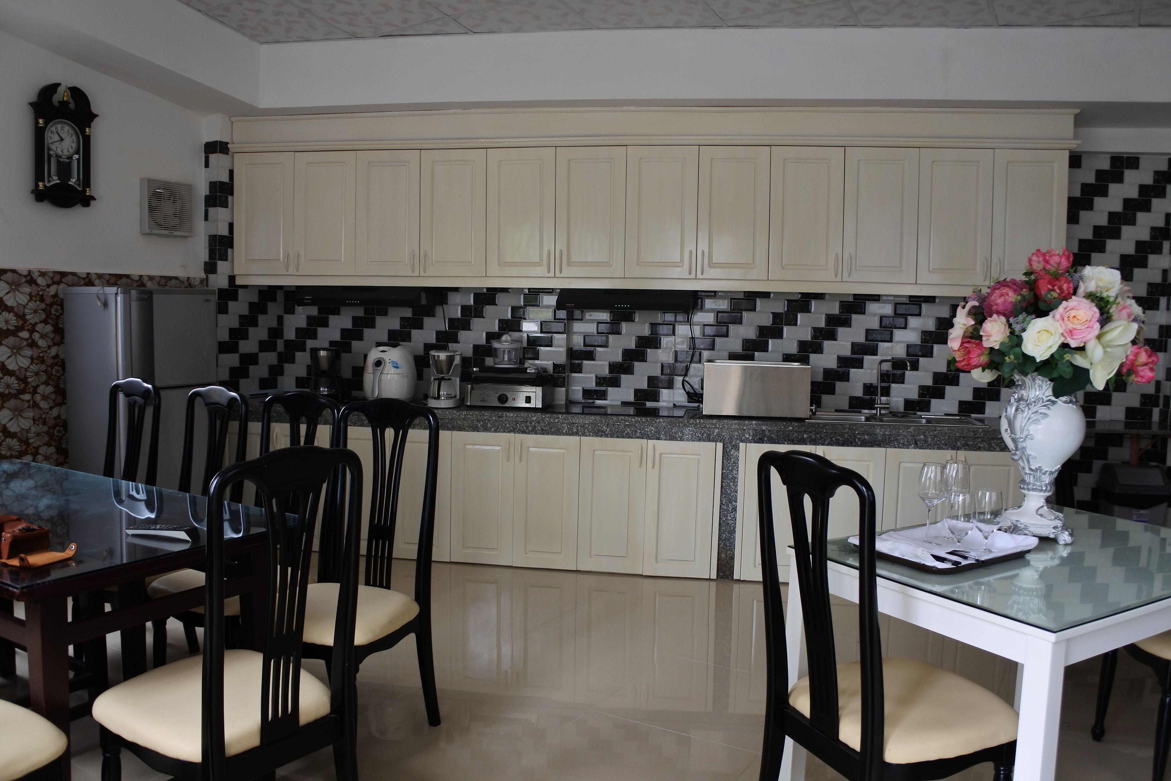 Cozinha com armários brancos, painel de azulejos, mesa de jantar com cadeiras e um vaso de flores sobre a mesa.
