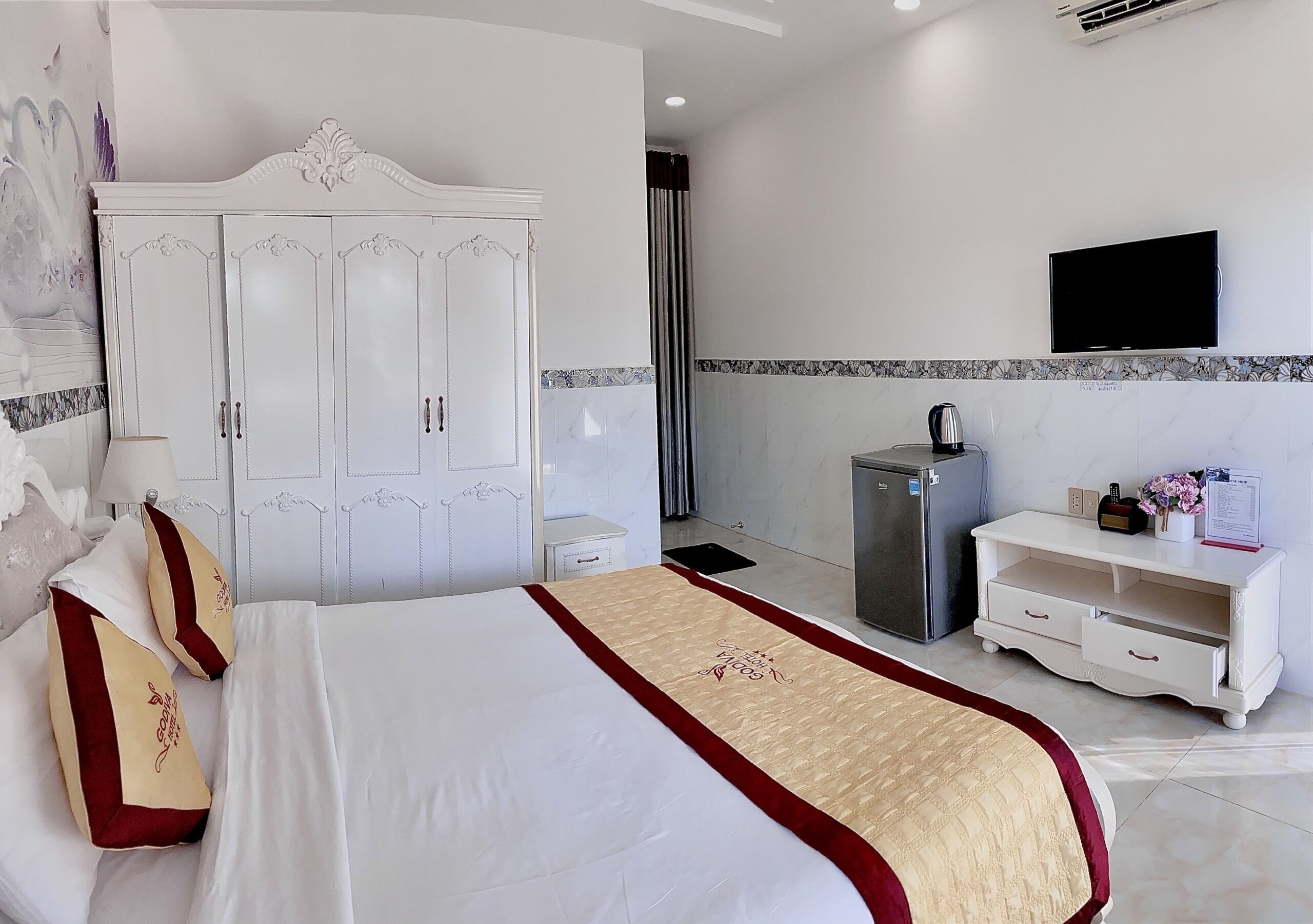 A hotel room with a large bed, a wardrobe, a television, a minibar, and a small desk.