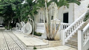 Um edifício com fachada branca, escadaria com balaústres brancos e um caminho de azulejos.