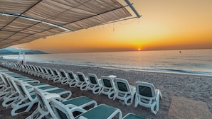 A beach with rows of white lounge chairs under a shaded area, facing the ocean at sunset. - Armas Gul Beach - All Inclusive (Kemer)