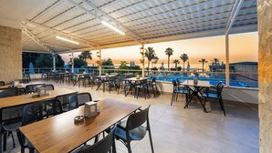 An outdoor dining area with tables and chairs, overlooking a pool and palm trees. - Armas Gul Beach - All Inclusive (Kemer)