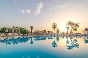 A swimming pool with lounge chairs and umbrellas, surrounded by palm trees and a clear sky. - Armas Gul Beach - All Inclusive (Kemer)