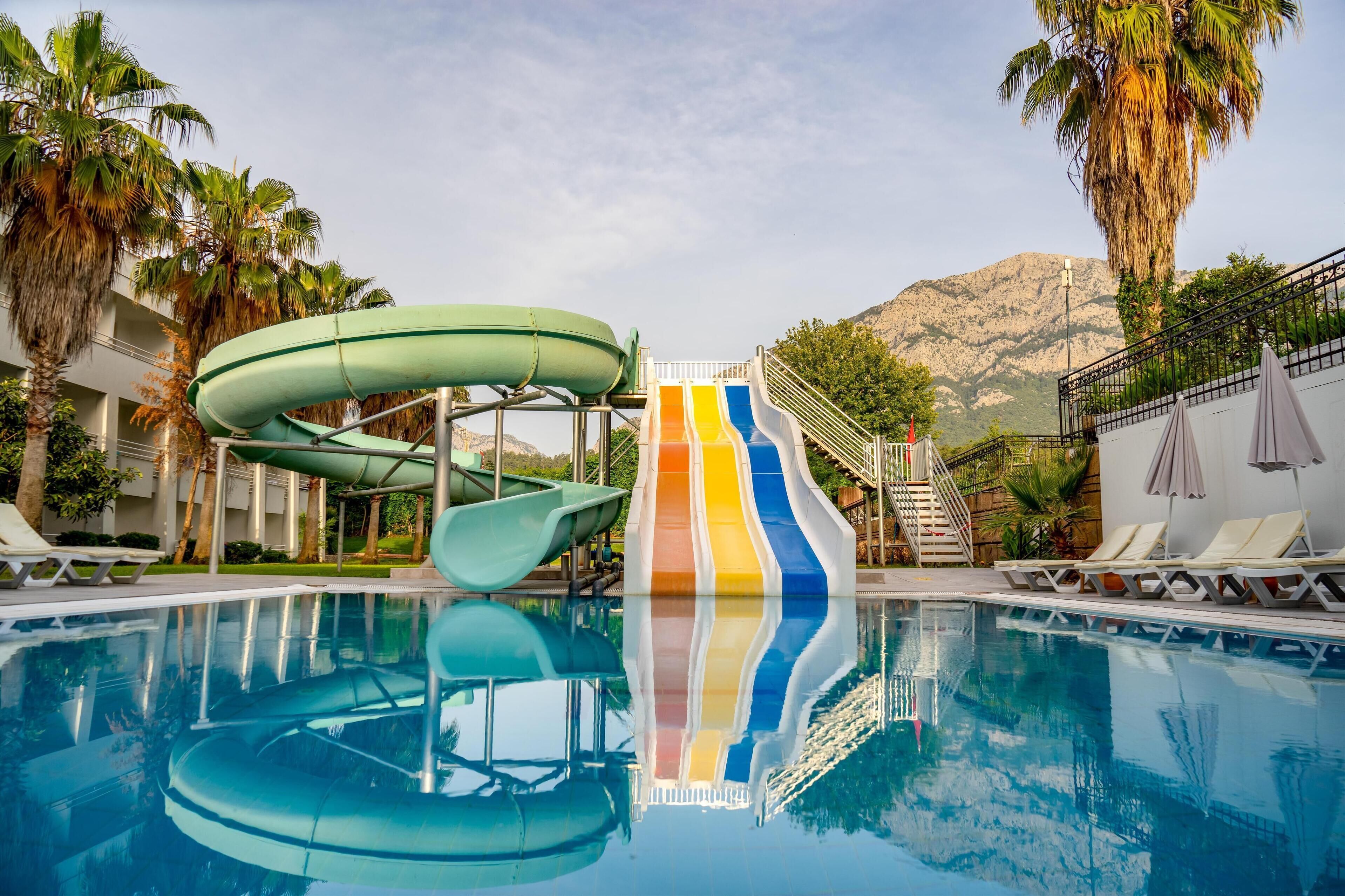 Una piscina con tobogán, palmeras y una montaña al fondo.
