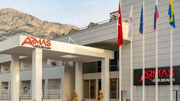 A building with 'ARMAS GULBEACH' signage, a covered entrance, and multiple flags.