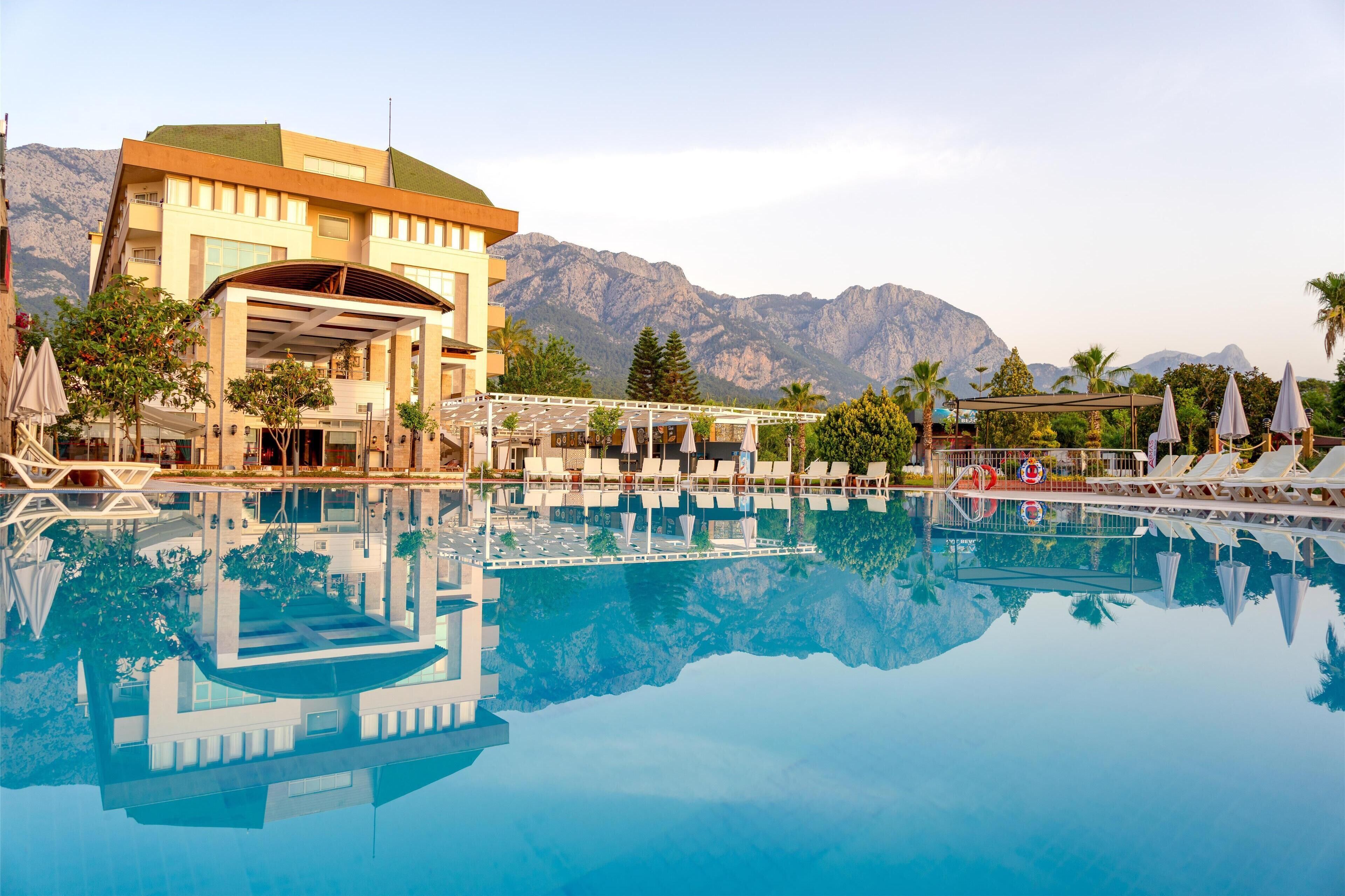 A hotel with a pool, lounge chairs, and a mountain backdrop.