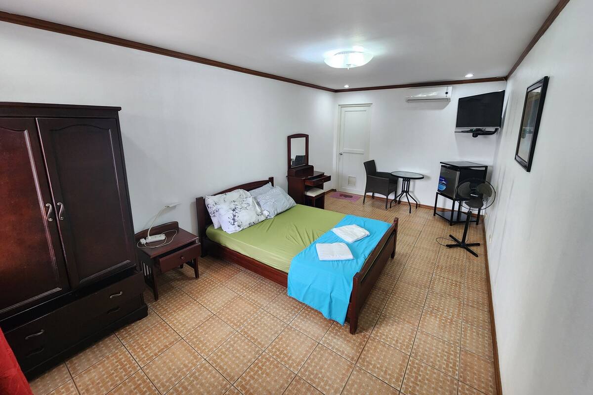 A hotel room with a bed, a desk, a chair, a wardrobe, and a TV.