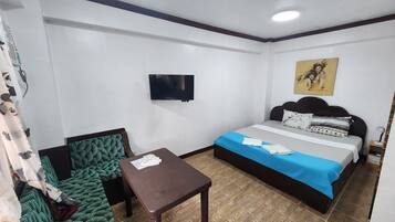 Habitación de hotel con cama, una mesita, una silla, televisión y un cuadro en la pared.