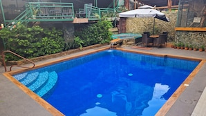 A rectangular pool with a wooden border, surrounded by a stone wall and potted plants. - MB's Garden Inn (Lapu-Lapu)