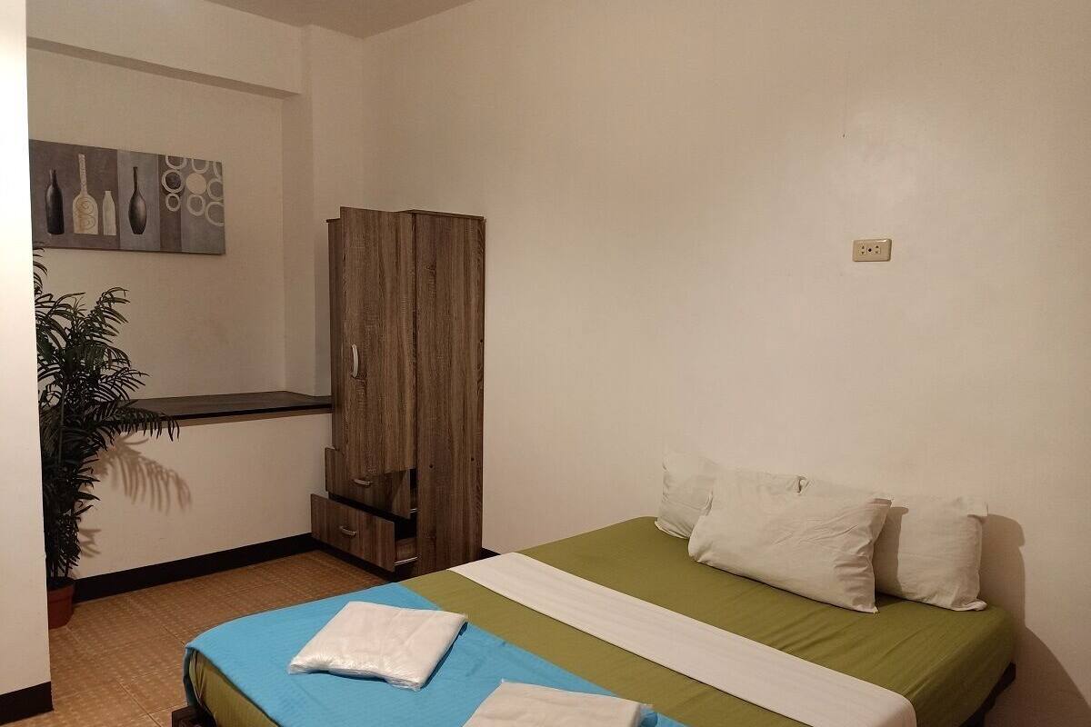 A bedroom with a bed, a wardrobe, a potted plant, and a wall-mounted artwork.