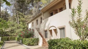 A two-story building with a staircase leading to the entrance, surrounded by greenery and trees. - Confluent Health Resort (Cofrentes)