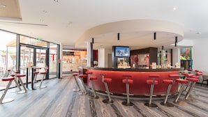 Un espace bar moderne avec un comptoir incurvé, de nombreux tabourets de bar rouges et un écran de télévision.