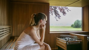 Un sauna avec des bancs en bois, une grande fenêtre donnant sur un paysage verdoyant et un appareil de chauffage pour sauna.