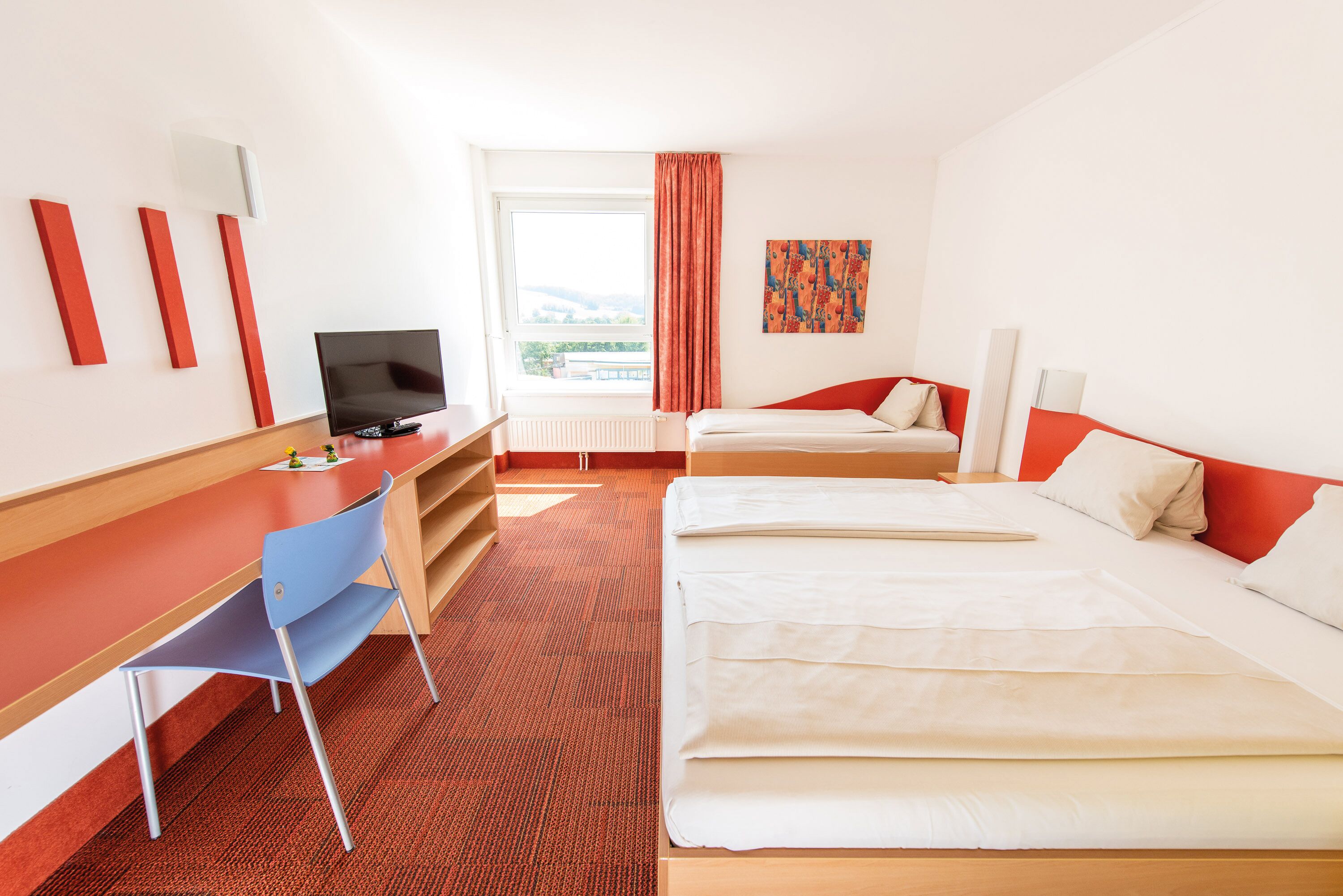 A hotel room with a bed, a desk, a chair, a TV, and a window with a view.