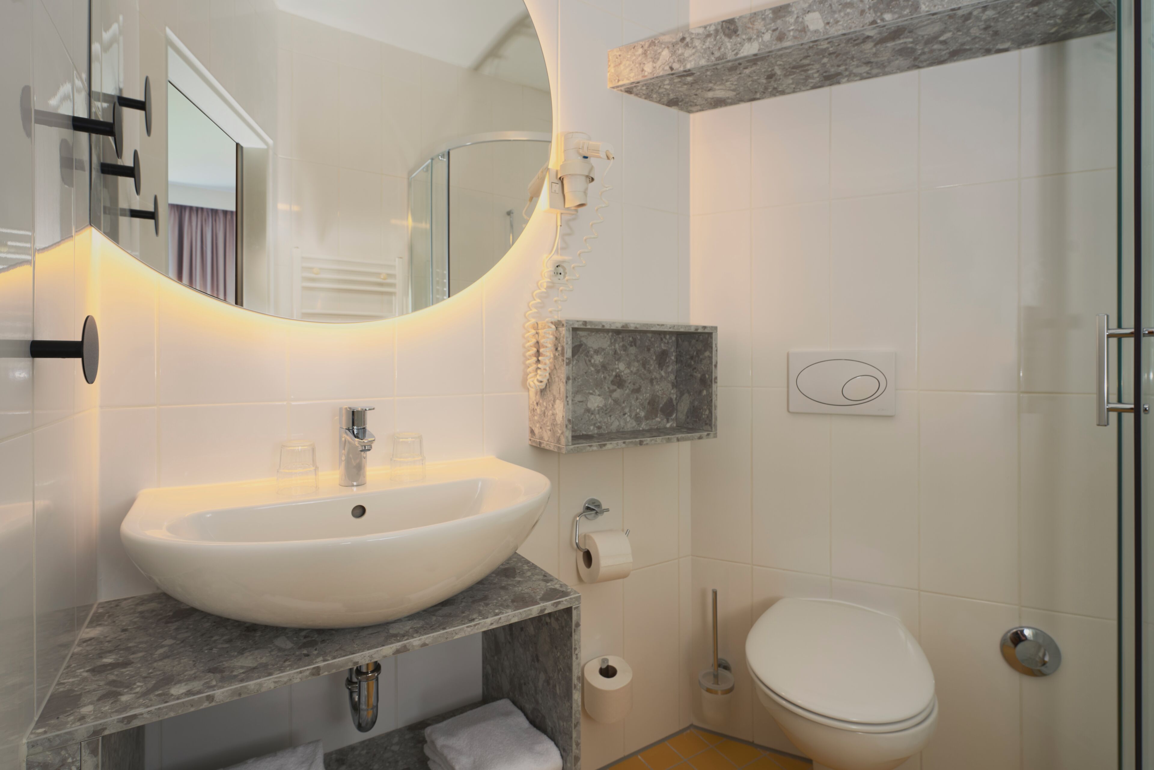 Un baño con un lavamanos ovalado grande, un inodoro, un espejo y una zona de ducha.