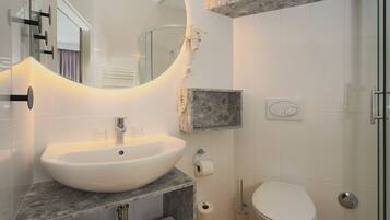 A bathroom with a large oval sink, a toilet, a mirror, and a shower area.